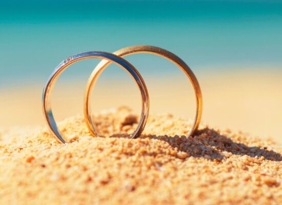 Pair of gold wedding ring bands jewelry in sand on tropical desert island beach