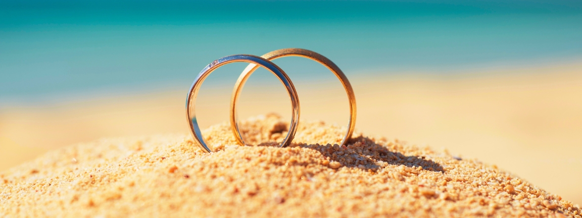 Pair of gold wedding ring bands jewelry in sand on tropical desert island beach