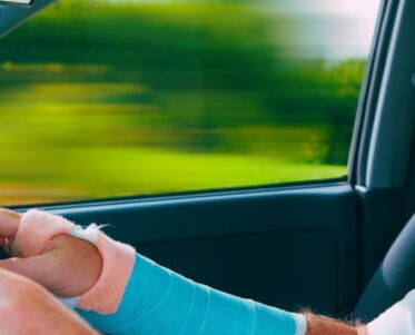 A middle aged man with a broken arm and no seatbelt driving a car.