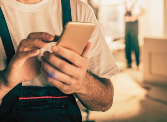 Happy male worker text messaging on smart phone while being in renovating home.