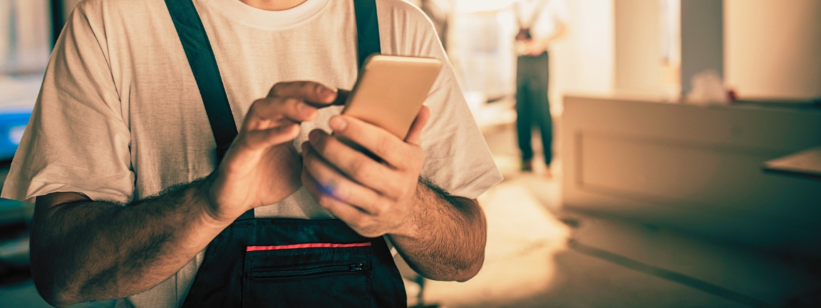 Happy male worker text messaging on smart phone while being in renovating home.