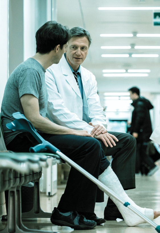 Mature man with broken leg, cast and crutches consulting a senior doctor. Shot in hospital corridor.