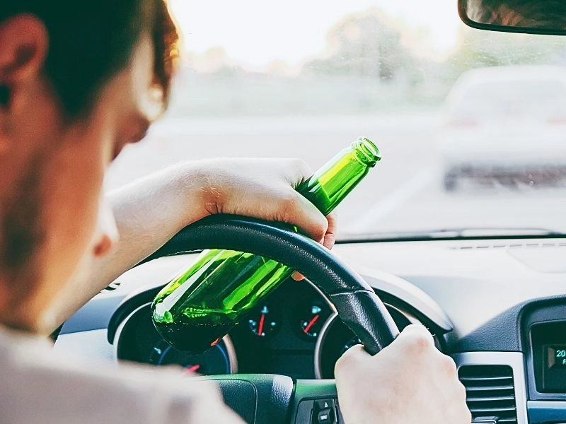 Drunk young man driving a car with a bottle of beer. Blackout Wednesday