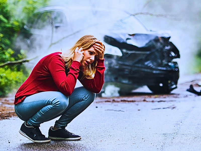 A frustrated young woman with smartphone making a phone call for help by the damaged car after a car accident. How to win a car accident case